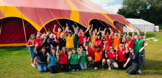 The team from Big Malarkey Festival in colourful t shirts in a group in front of a big red and yellow marquee.