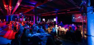 Audience watching a conference stage which is bathed in red and purple light.