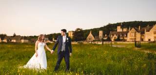 A newlywed couple walk through yellow wildflowers with Ellenborough Park in the distance