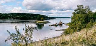 Utsikt over Glomma fra Furuholmen. To gamle båter ligger til kai langs ei flytebrygge.