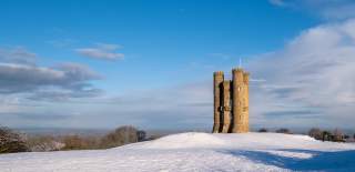 Historic Broadway Tower stands overlooking snow covered countryside on a bright winter's day