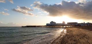The sun sets behind South Parade Pier, with Southsea beach and sea in the foreground