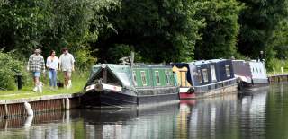 Three friends with a dog walking along the canal towpath past moored canal boats