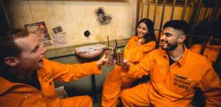 Group with cocktails wearing orange jumpsuits in a cell - credit Alcotraz