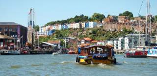 A Bristol Ferry Boat sailing eastwards on Bristol's Harbourside, with the SS Great Britain and colourful houses of Cliftonwood in the background - credit Visit West