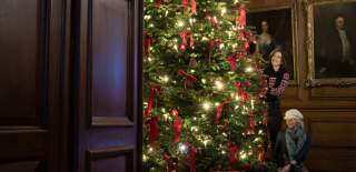 Two people decorate a very large Chritsmas tree with red bows and lights