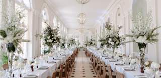 Long tables stretch the length of the Orangery at Blenheim Palace, decorated with white linen, place settings and large vases of white flower arrangements