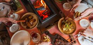 People serving themselves at a communal table with an open grill and fire at Wild restaurant in BULL Burford