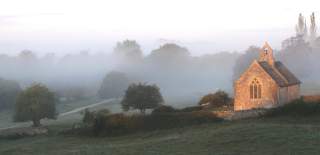 St Oswald's Church in Widford with sun on the building and an early morning mist (photo by Helena Sylvester)