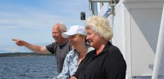 En mann og to kvinner står ved relingen på en båt og peker ut mot havet