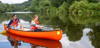 A couple in a bright orange canoe paddle down the rive at Ross on Wye in the Forest Of Dean & Wye Valley