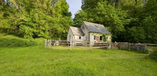 A Cotswold stone cottage surrounded by a wooden fence and backed by trees at Westley Farm