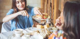 A woman in a blue dress takes a scone from a cake stand, which is filled with sandwiches, scones and cakes, in the Cotswolds