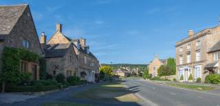 The wide High Street in Broadway with honey-coloured houses on both sides and bright blue sky with whisps of clouds above