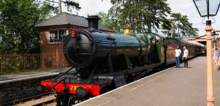 Two men stand on Broadway station platform looking at a Gloucestershire Warwickshire Steam Railway train