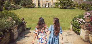Two women walking arm in arm towards Bourton House