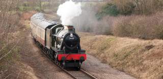 Gloucestershire Warwickshire Steam Railway train coming through the countryside with a big plume of steam