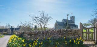 Swinbrook Church with stone wall and daffodils in the foreground