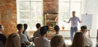 A person talks to a group of people seated in rows at a business event