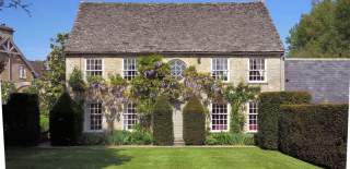 Wisteria covers a Cotswold stone building set amongst manicured trees at Bruern Cottages in the Cotswolds