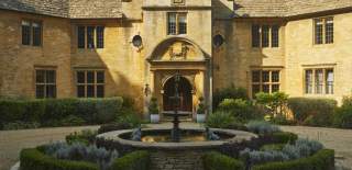 A circular fountain surrounded by topiary creates a stunning centrepiece in front of the entrance to the impressive honey-coloured stone Foxhill Manor