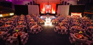 A large room with stage and large screen, and tables dressed for a gala dinner at Cheltenham Racecourse