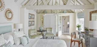A light and airy bedroom with white washed rafters over a large bed with cosy blanket and pillows