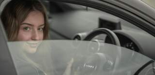 Photograph of a woman behind the wheel of an Audi, looking out of a slightly opened side window