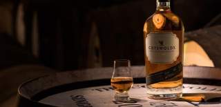 A glass and bottle of Cotswolds Single Malt Whisky on a whisky barrel