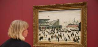 A person standing looking at the famous L S Lowry painting, Going To The Match.