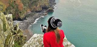 Lady sat on rock overlooking Valley of the Rock and the coast