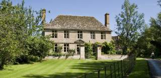 A large country house made of Cotswold stone set amongst trees with an extensive lawn at Manor Farm