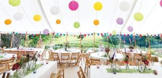 A marquee with brightly coloured ball lights hanging above tables decorated with fresh flowers at Cowley Manor