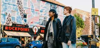 Two people stand on Victoria Road next to a venue called 'Rockpoint Records' that has pink and blue street art