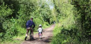 Father and daughter cycling down a leafy bridleway