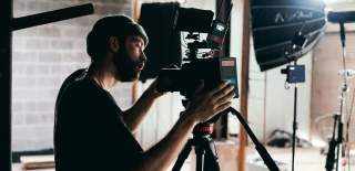 A man in a beanie hat using a film camera in a warehouse setting.