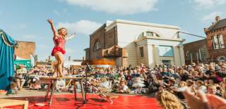 A contortonist performer in a red leotard raises her arms on stage to an audience at Freedom Festival in Hull.