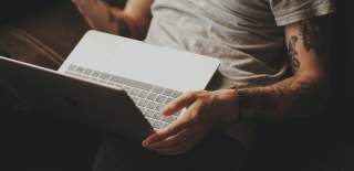Photograph of a person in a white t-shirt with a laptop tilted upwards on their lap