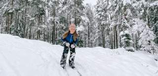 Barn som står på ski ned en bakke i skogen. Foto.