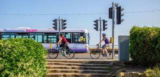Photograph from Southsea Seafront, showing two cyclists going right to left from the viewer's perspective, whilst a First Solent bus passes in the opposite direction.