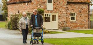 A couple walking the grounds at Broadgate Farm Cottages in East Yorkshire. The man is walking with the aid of a rollator.