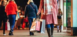 Lady dressed in light pink jacket and scarf carrying a bundle of Christmas shopping