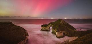 The pink and green Northern Lights filling the skies above the famous Drinking Dinosaur cliff stacks at Flamborough with the seals nestled in the bay for shelter.