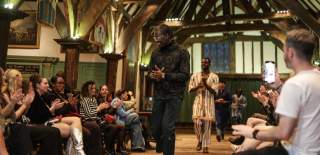 Seguntuyi Onakoya walks down a runway at Ferens Art Gallery whilst the audience claps. He smiles at the onlookers and a male model follows him on the runway.