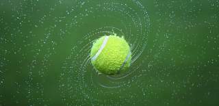 Photograph showing a spinning wet tennis ball, with water droplets flying off it