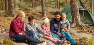 Familie på tur i skogen hvor de griller pølser.