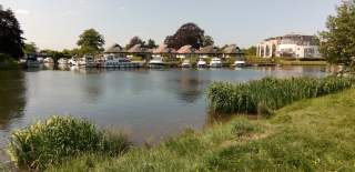A view of Chertsey Marina over the water of the river Thames. Small boats are moored to the far bank.