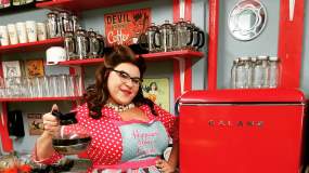 A South Press server holds up a fresh cup of joe as she poses next to a red vintage fridge.