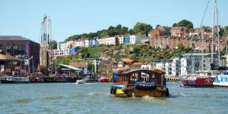 A Bristol Ferry Boat sailing eastwards on Bristol's Harbourside, with the SS Great Britain and colourful houses of Cliftonwood in the background - credit Visit West