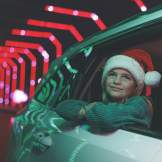 A young girl wearing a Santa hat looks out a car window at a festive drive-through Christmas light display during a holiday vacation in Branson, Missouri